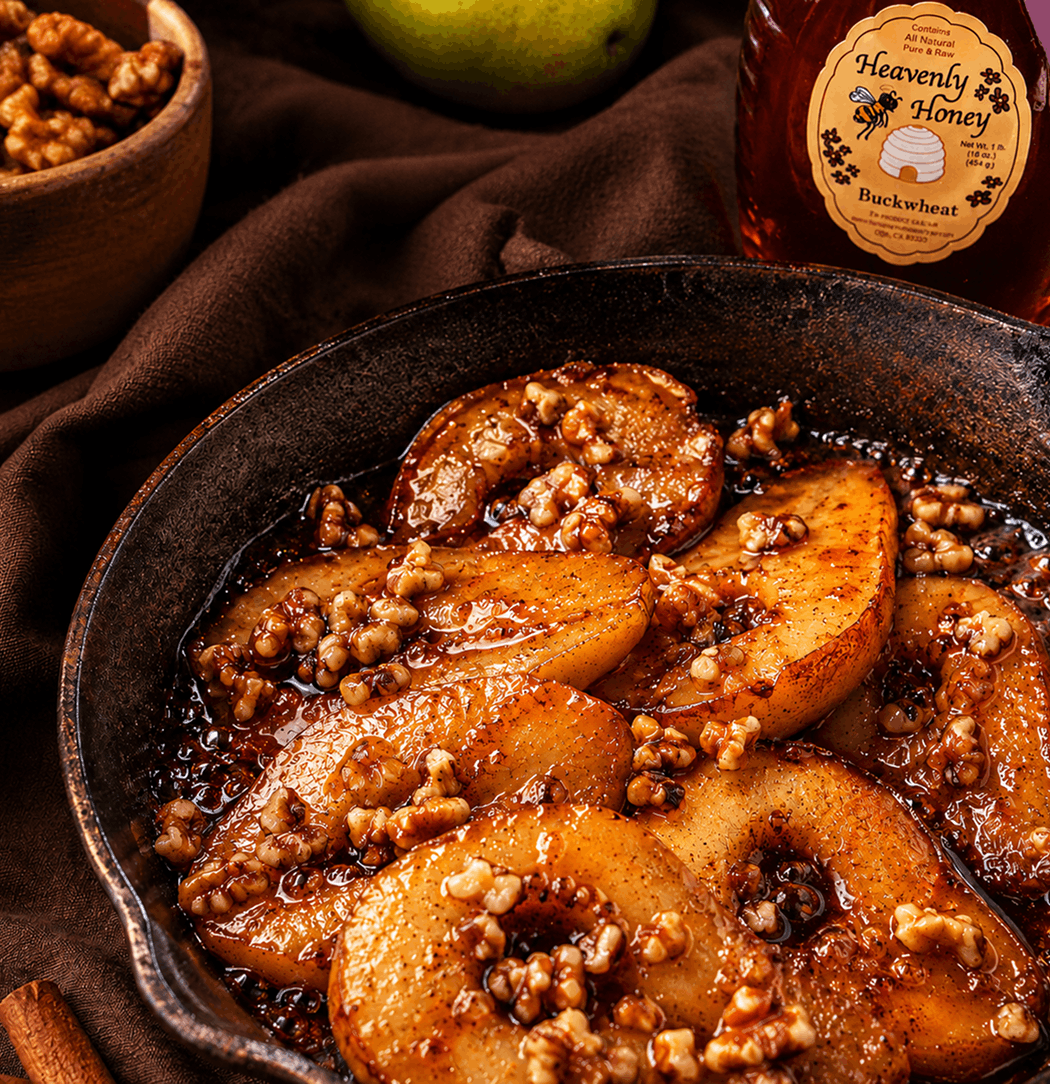 Slices of tender, caramelized pears bubbling in a rustic skillet with a rich, dark amber buckwheat honey glaze, topped with toasted chopped walnuts and a sprinkle of cinnamon under warm kitchen lighting.