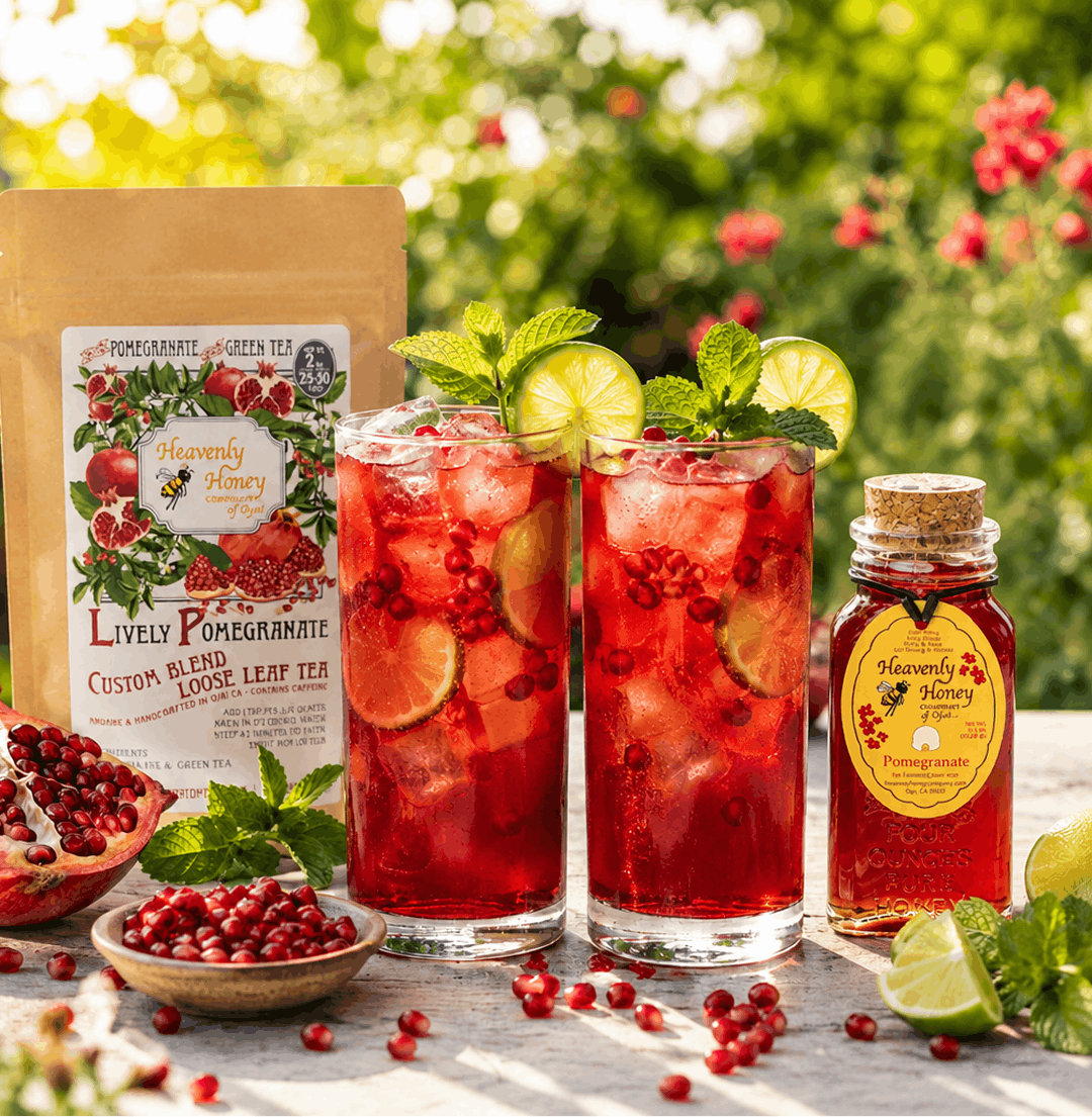 Two tall, effervescent glasses of ruby-red Ojai Pollinator Pomegranate Honey Spritzer iced tea on a sun-drenched garden table, filled with ice cubes, fresh pomegranate seeds, lime wheels, and vibrant green mint sprigs.