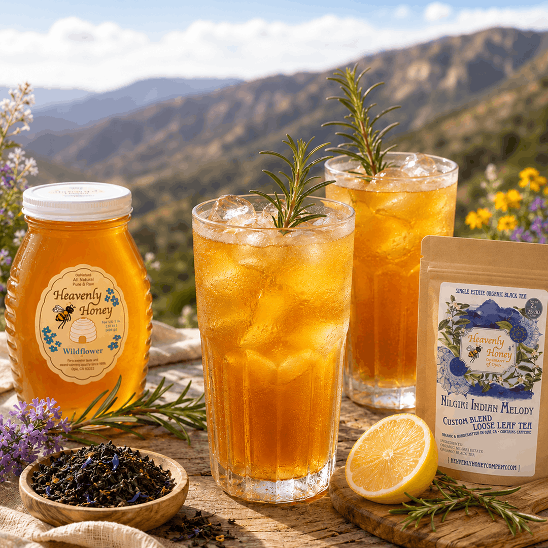 Two frosted glasses of amber-colored Five-Mile Forager's Nilgiri Tea Cooler filled with ice and fresh rosemary sprigs, resting on a sun-drenched wooden picnic table with a soft-focus background of wild canyon hillsides.