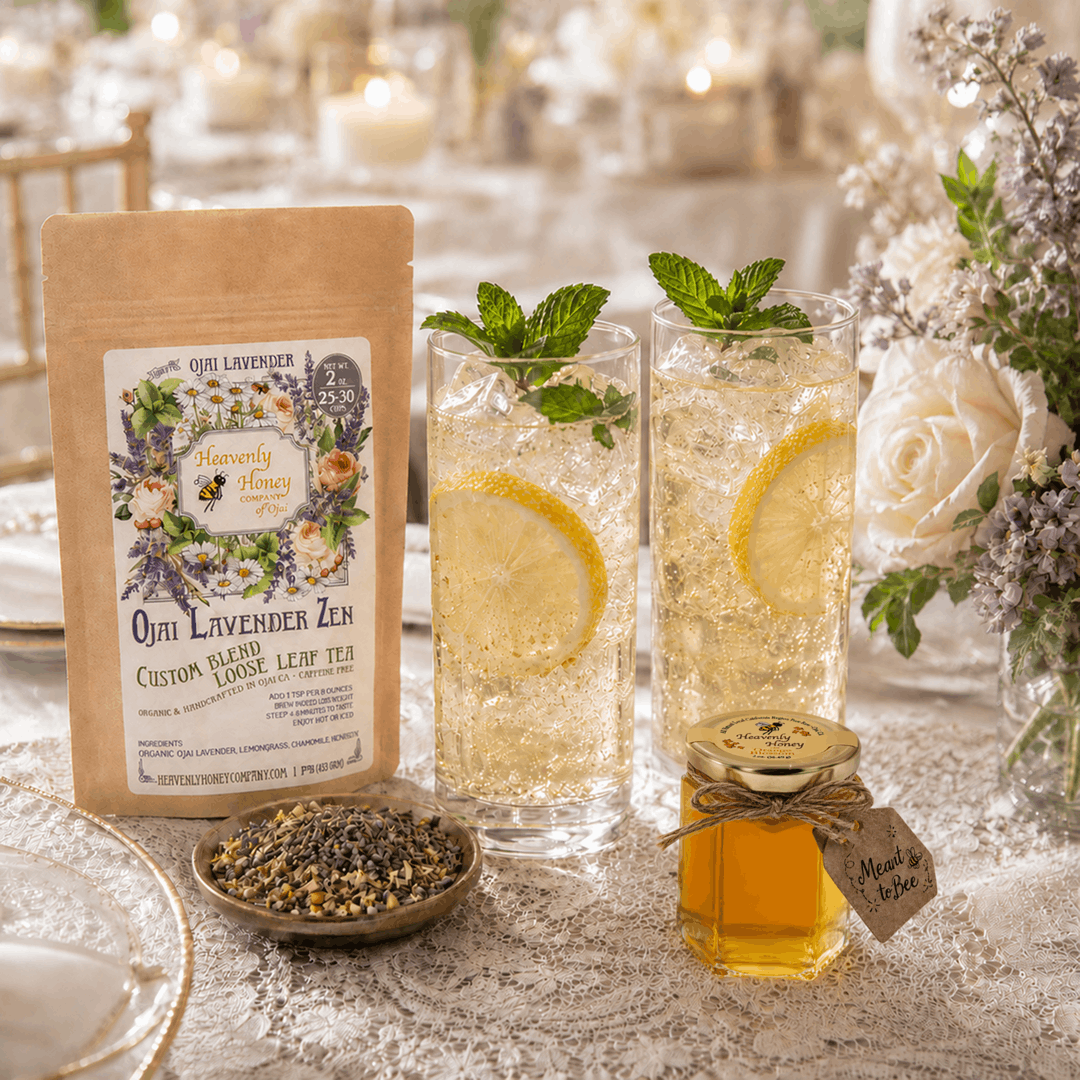 Two elegant, effervescent glasses of Ojai Meant-to-Bee Lavender Zen Spritzer filled with ice, lemon wheels, and mint garnishes, resting on a lace-covered wedding reception table next to a tiny 2oz hexagonal honey jar favor with a rustic "Meant to Bee" tag.